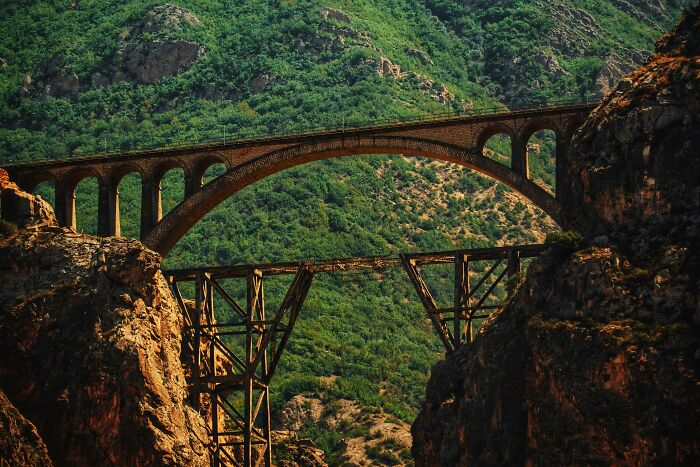 Rustic iconic landmark bridge spanning rocky cliffs with lush green mountains in the background, showcasing popular world myths.