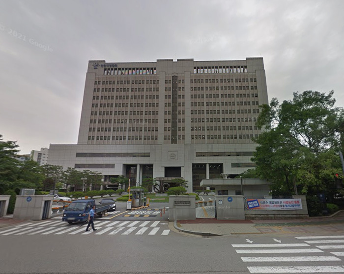 Downtown LA street view with large building and a man crossing near parked vehicles on a cloudy day.