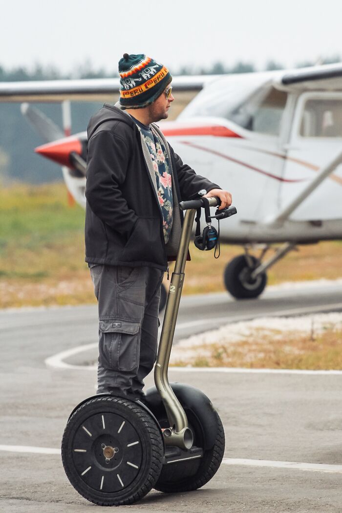 Homem usando um chapéu de inverno colorido andando em uma scooter Segway perto de um pequeno avião, ilustrando um cenário de desastre de relações públicas.