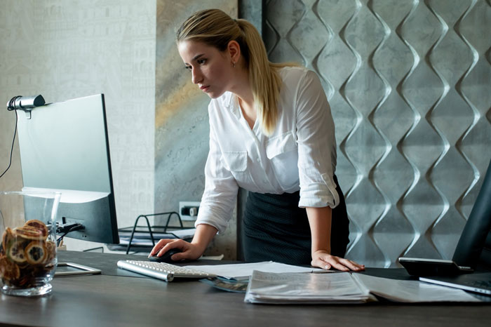 Woman at office desk working on computer, illustrating work-life balance challenges faced by a cynic boss.