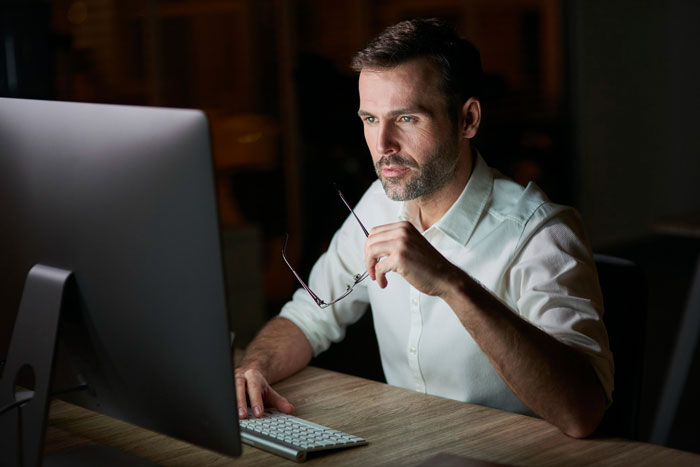 Man in a white shirt focused on a computer screen late at night, reflecting on work-life balance and its challenges.
