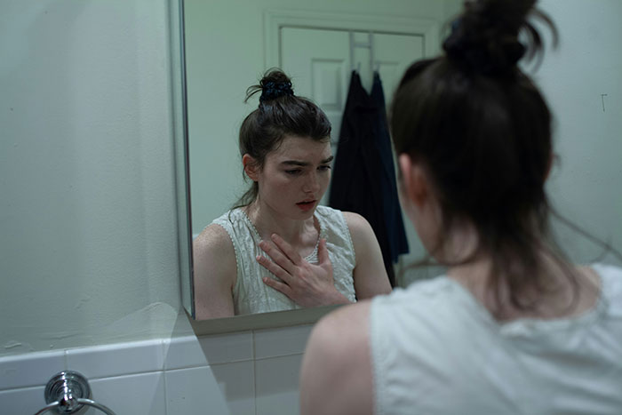 Young woman with a concerned expression looking into a bathroom mirror, experiencing an eerie and unexplained moment.
