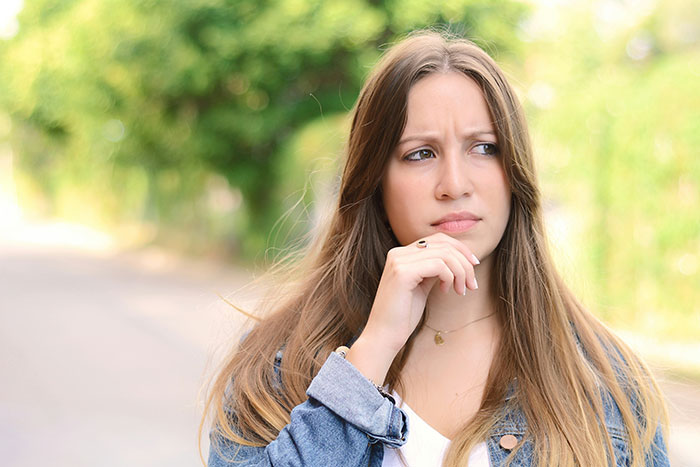 Young woman outdoors with a thoughtful expression, reflecting on eerie and unexplained things experiences.