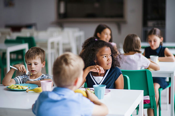 Children sitting at tables in a cafeteria, some looking distracted, evoking eerie and odd unexplained experiences.