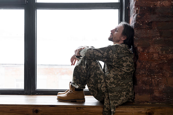 Man in camouflage clothing sitting by a window, appearing deep in thought about eerie unexplained experiences.