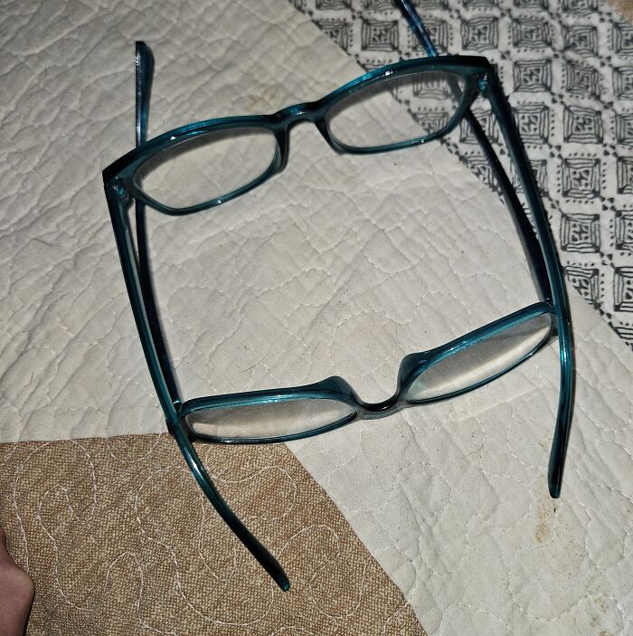 Two pairs of teal glasses overlapping on a quilted surface, evoking eerie and odd unexplained experiences.