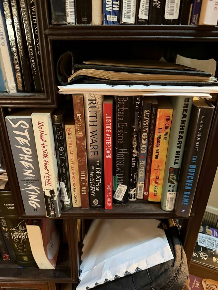 Books on a wooden shelf with eerie, odd, and thought-provoking themes about people experiencing unexplained things.