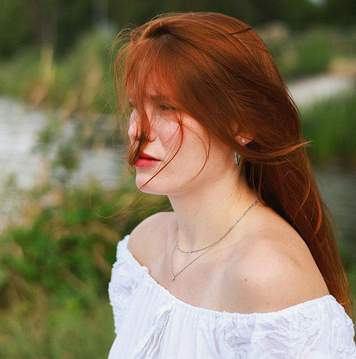 Young woman with red hair outdoors, evoking eerie and odd vibes linked to unexplained experiences stories.