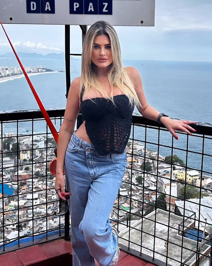 Influencer posing in casual black top and jeans against a coastal city backdrop after Disney World outfit complaints.