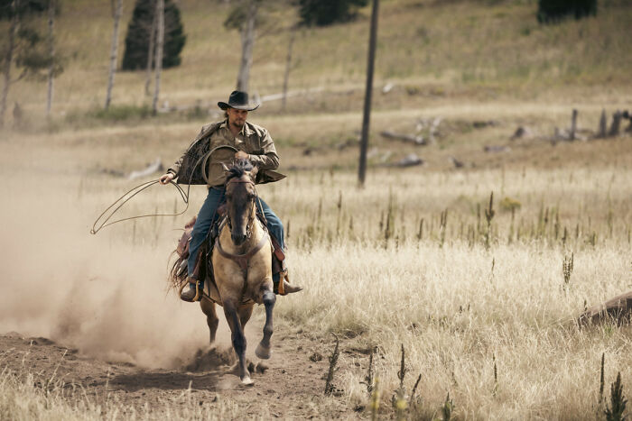 Cowboy riding a horse at full speed through a dusty field, capturing the Yellowstone infamous location atmosphere.