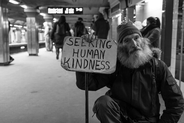 Homeless man holding a sign seeking human kindness in a subway station, illustrating moments people destroyed their own lives.