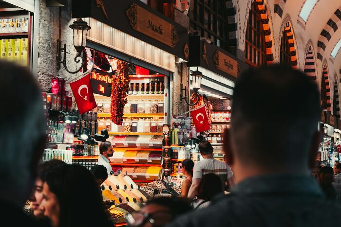 Busy market scene with Turkish flags and spice stalls, reflecting vanished truths from people’s home countries shared online.