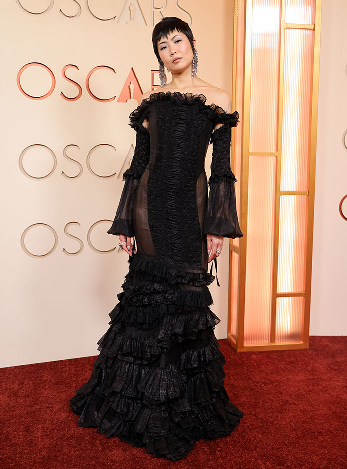 Model in a sheer black ruffled gown posing at the Oscars, showcasing outrageous and disastrous looks from the event.