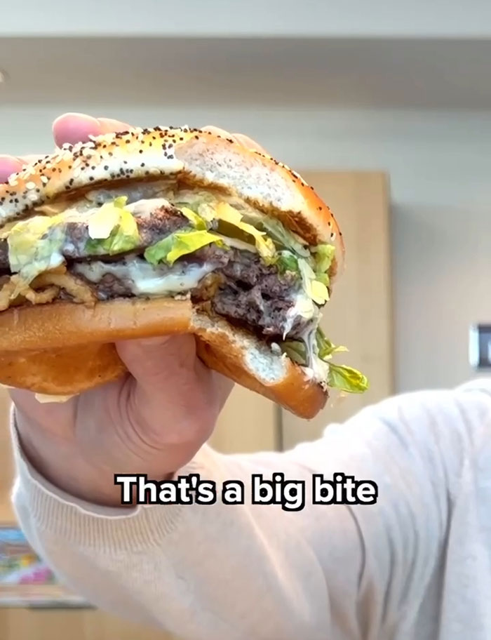 Close-up of a hand holding a large burger with lettuce and cheese, highlighting Wendy's burger battle in fast food.