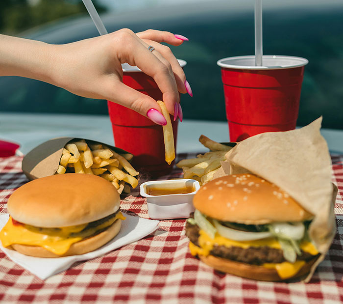 Hand dipping a French fry into sauce with burgers, fries, and drinks on a checkered table, Wendy's burger battle theme.