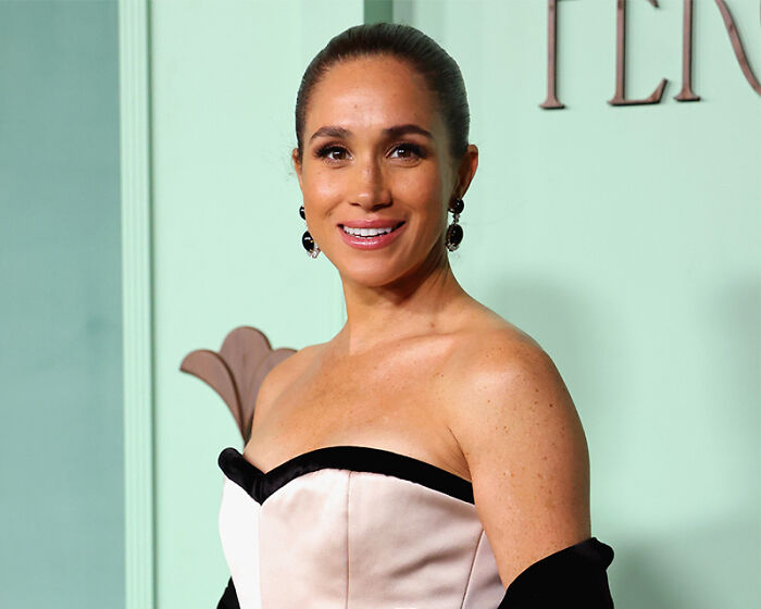 Meghan Markle smiling in a strapless dress, related to lip reader revealing senior royals' brutal takedown.