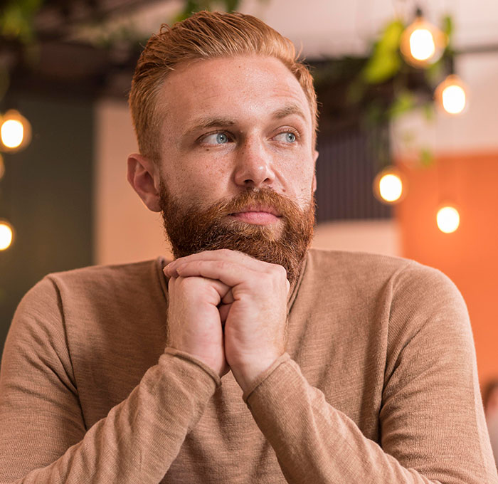 Bearded man in a brown sweater looking thoughtful, representing men sharing moments that changed their Red Pill mindset.