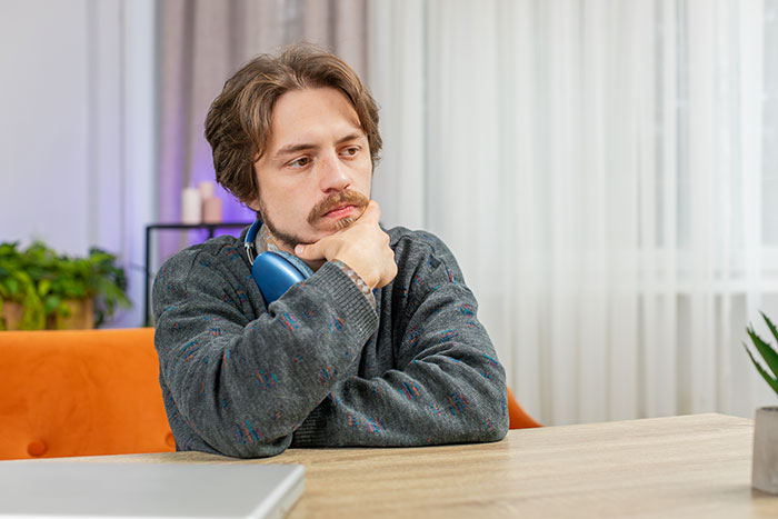 Thoughtful man with headphones around neck sitting at table, reflecting on moments that made him drop the Red Pill mindset.