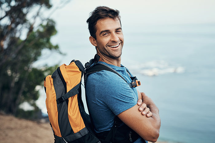 Man with backpack smiling outdoors by the sea, symbolizing men dropping the red pill mindset and personal growth.