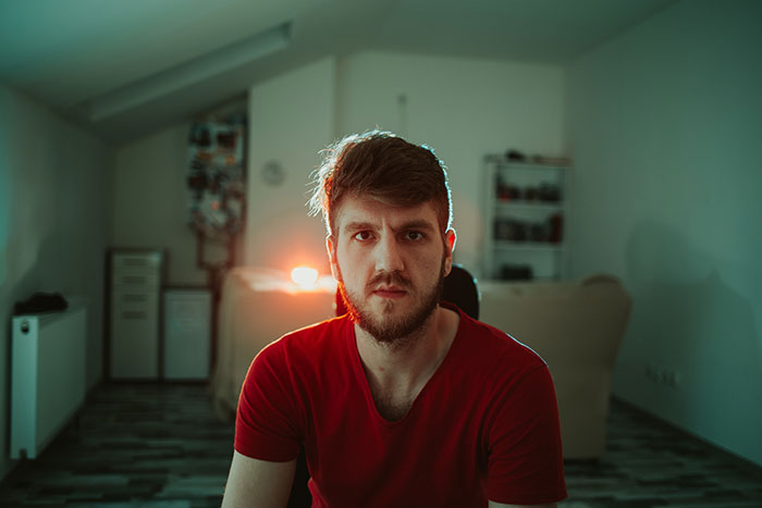 Young man in a red shirt sitting indoors with serious expression reflecting on dropping the red pill mindset.