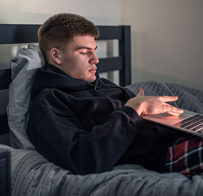 Young man in casual clothes lying on bed using laptop, reflecting on dropping the red pill mindset.