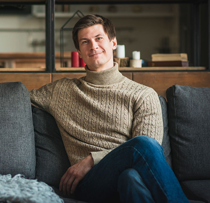 Man sitting on a couch smiling thoughtfully, reflecting on the moment he dropped the red pill mindset.