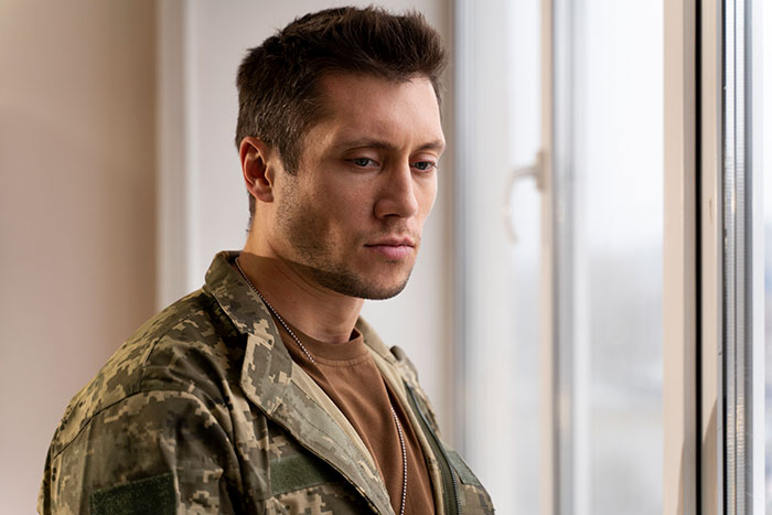 Young man in military uniform looking thoughtful by a window, reflecting on dropping the red pill mindset.