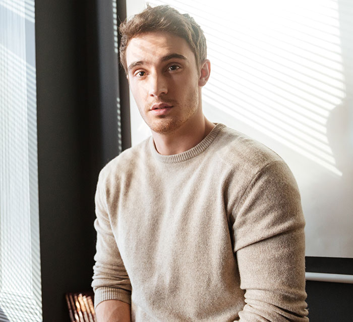 Young man in beige sweater reflecting on experiences that made him drop the red pill mindset in a sunlit room.