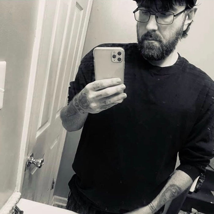 Man with glasses and tattoos taking a mirror selfie while reflecting on owning the world's tiniest package and issuing an apology.