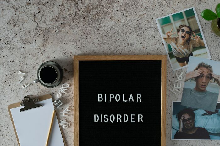 Black felt board with bipolar disorder text, photos of stressed and happy people, clipboard, coffee cup, and letters on a table.