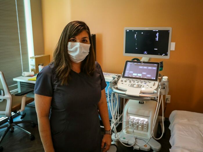 Female medical professional wearing a mask in an examination room with brain malfunction diagnostic equipment nearby