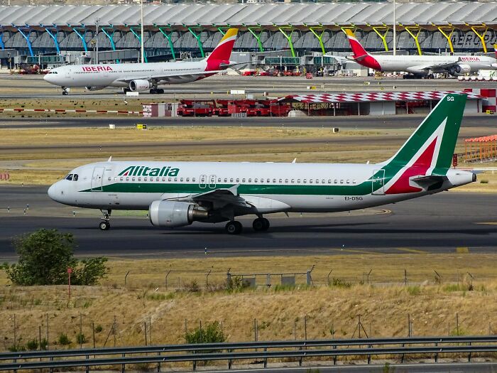 Alitalia airplane taxiing on runway at busy airport, illustrating crazy things people did for love involving travel.