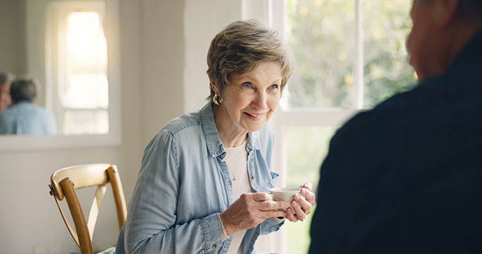 Older woman planning a spite trip, holding a cup and smiling, while reacting to son and daughter-in-law rejection.