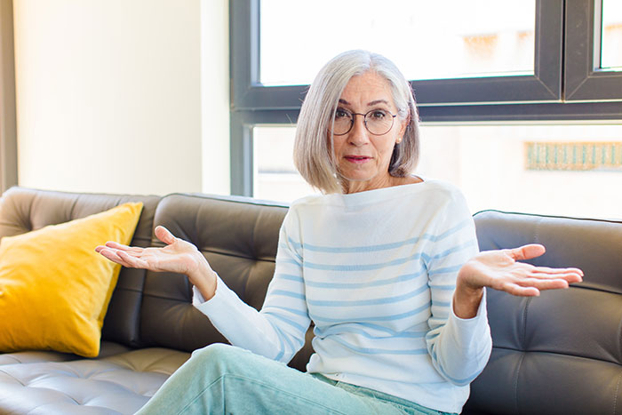 Older woman looking confused and frustrated, sitting on a couch and expressing emotion after family rejection.