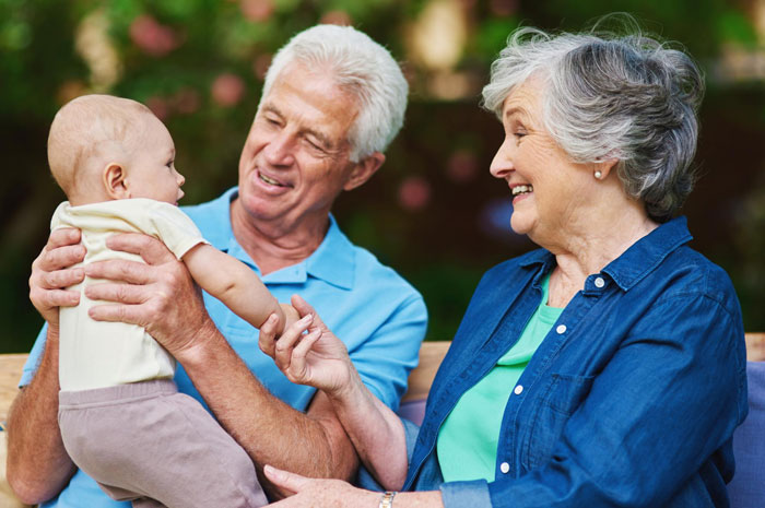 Elderly in-laws happily interacting with baby outdoors, symbolizing new mom anxiety during visits and family tension.