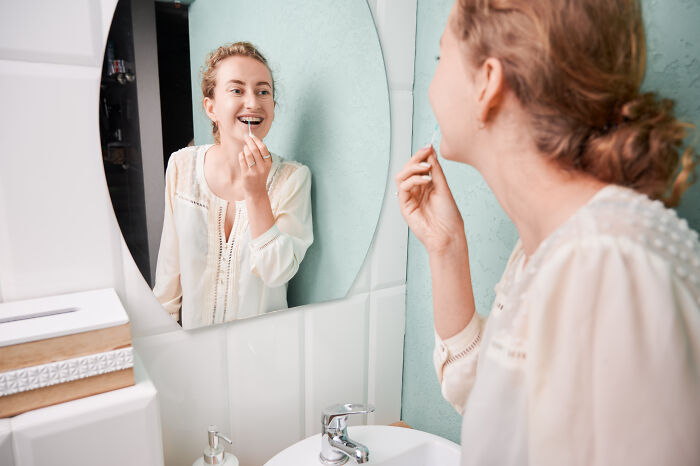 Young woman smiling while applying lipstick in bathroom mirror, capturing a moment like this generation's moon landing discovery.