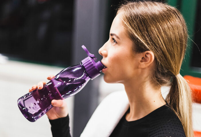 Young woman drinking water from a purple bottle during workout, representing this generation’s impactful discoveries.