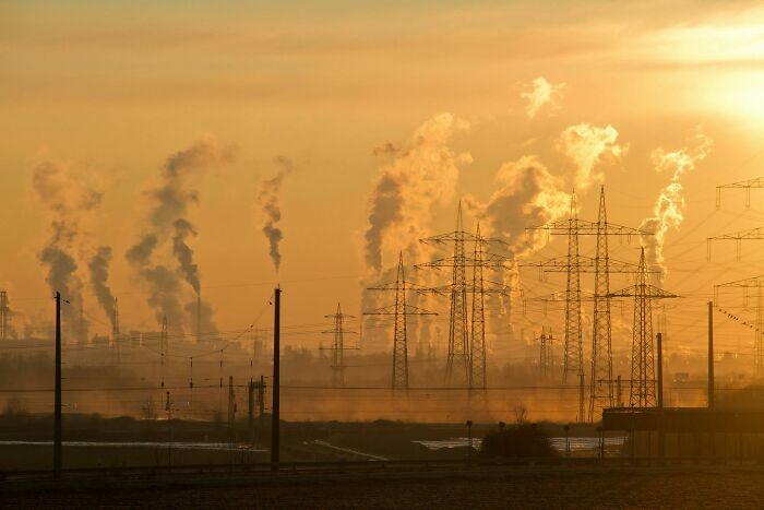 Industrial smokestacks emitting pollution at sunset with power lines, symbolizing wild discoveries impact on environment.