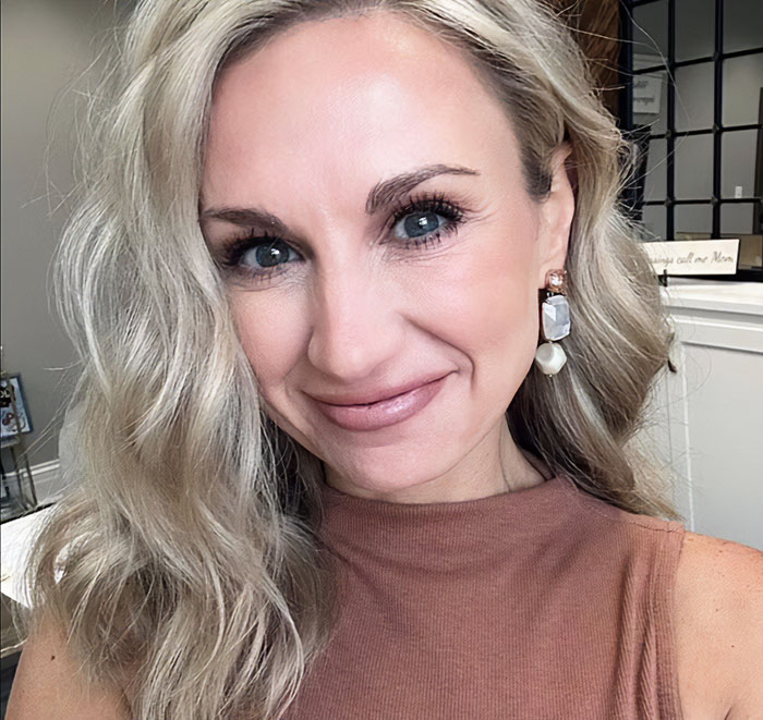 Former Louisiana mayor smiling indoors with blonde hair, wearing earrings and a sleeveless brown top in a home setting.
