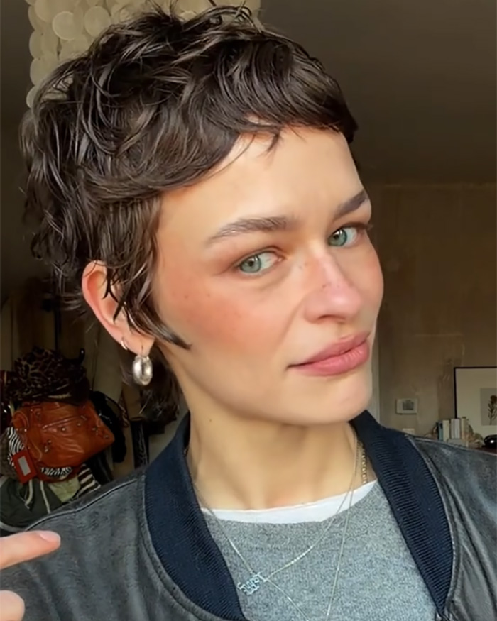 Model with short hair wearing silver hoop earrings and layered necklaces, addressing fashion brand plagiarism with AI photos.