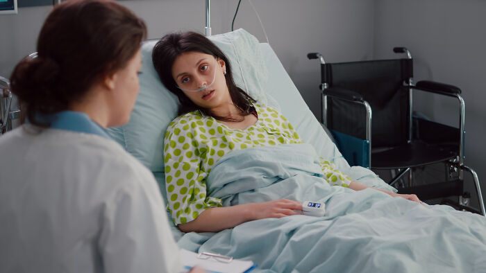 Young woman in hospital bed with oxygen tube talking to doctor, showing the nasty side of a tough situation.