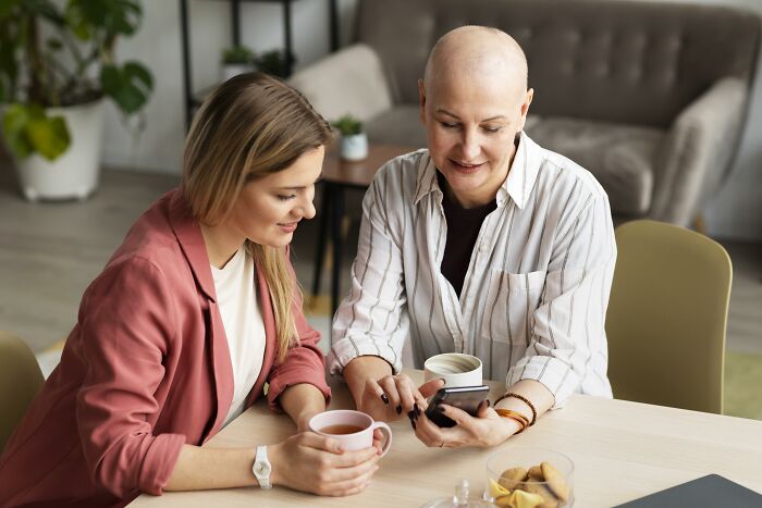 Two women sitting together at a table, sharing a moment while looking at a phone, capturing the nasty side of people.