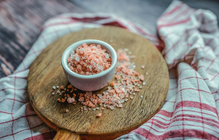 Close-up of pink Himalayan salt crystals in a white bowl on a wooden board, illustrating bizarre culture shock food experiences.