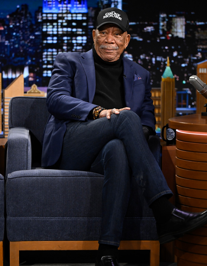 Morgan Freeman seated on a talk show set wearing a navy blazer and black cap discussing felonies.