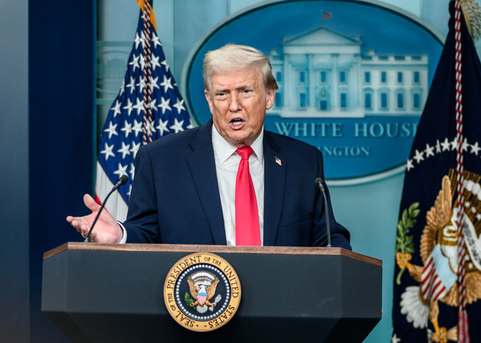Former President Trump speaking at the White House podium with American flags, discussing felonies and controversies.