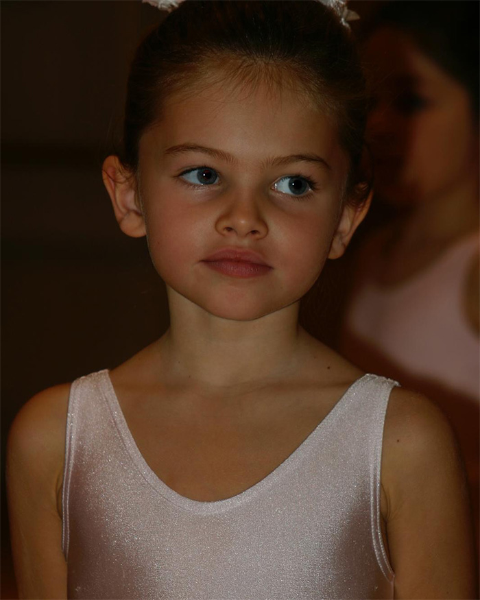 Young girl with blue eyes wearing a glittery pink dress, representing the most beautiful girl in the world in a candid portrait.