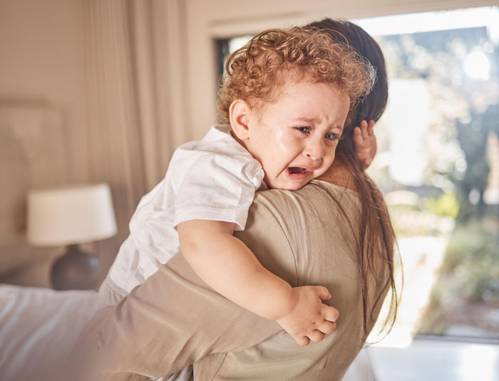 Woman holding and comforting crying toddler nephew, highlighting breakup and harassment challenges after relationship ends