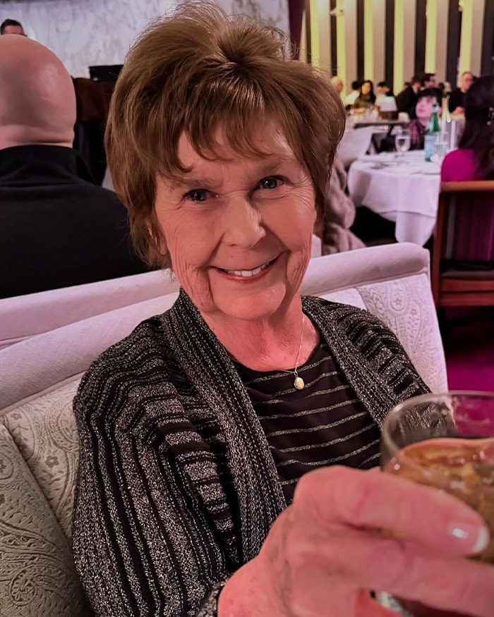 Elderly woman smiling in a restaurant, holding a glass, related to FBI analysis of Nancy Guthrie case theories and new lead.