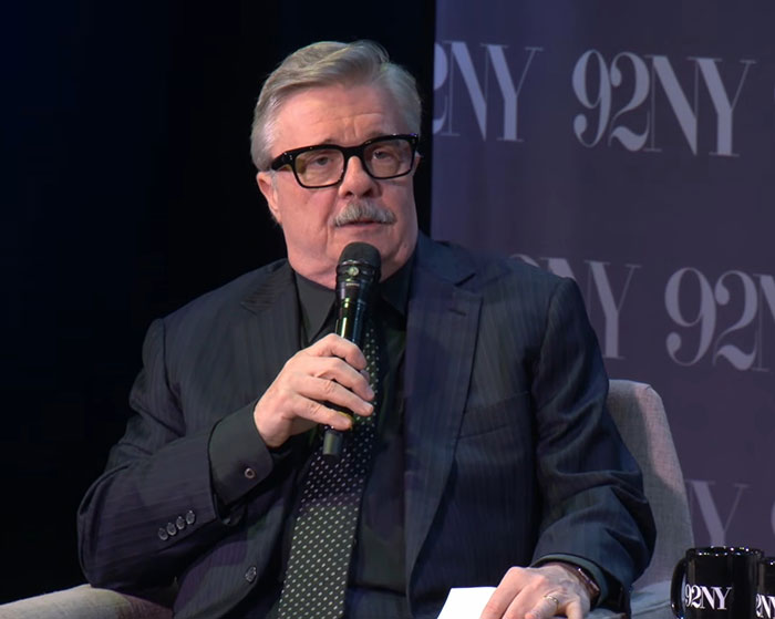 Acting legend in a dark suit speaking into a microphone during a 92NY event on stage with a black backdrop.
