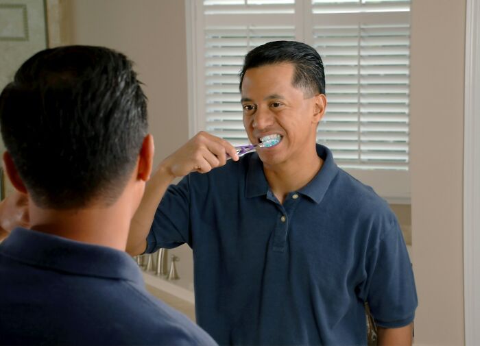 Man brushing teeth in the bathroom mirror, illustrating a daily life hack related to personal hygiene routines.
